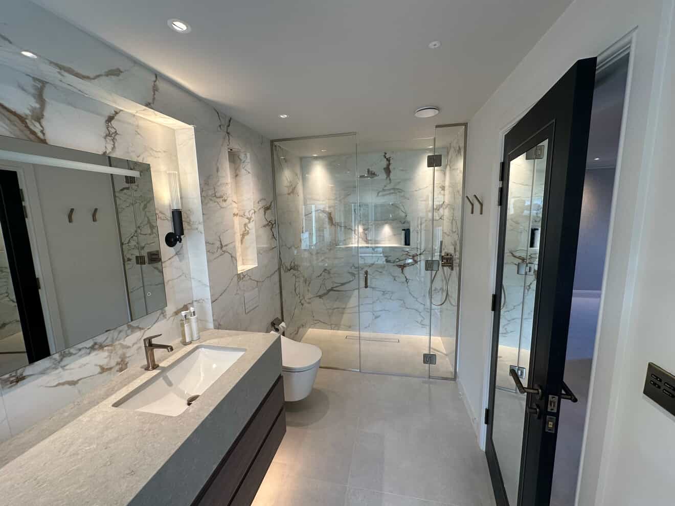 Marble walk-in shower room with recessed LED downlights, backlit niche and glass shower enclosure