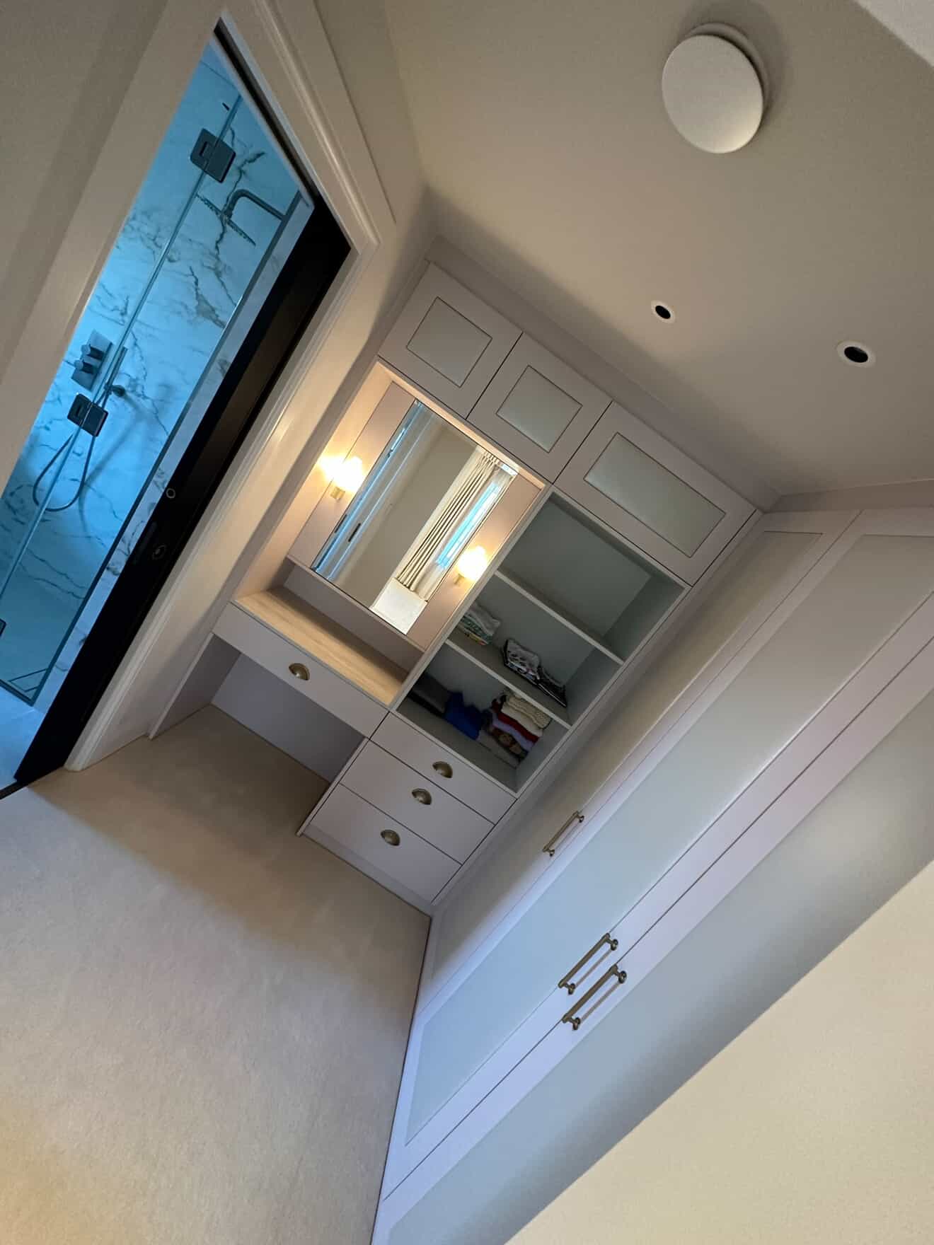 Dressing room with illuminated vanity mirror, built-in storage and recessed downlights